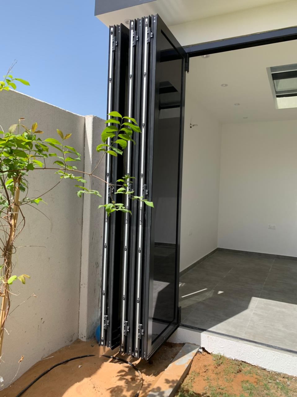 Frameless Folding Doors 7 Black bi-folding doors stacked open beside a garden - Zealcon